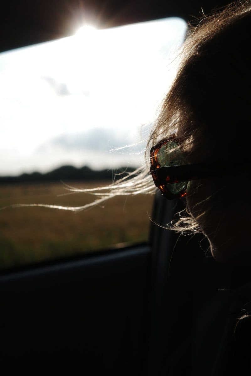 Sun through a car window lights a woman’s wind-blown hair