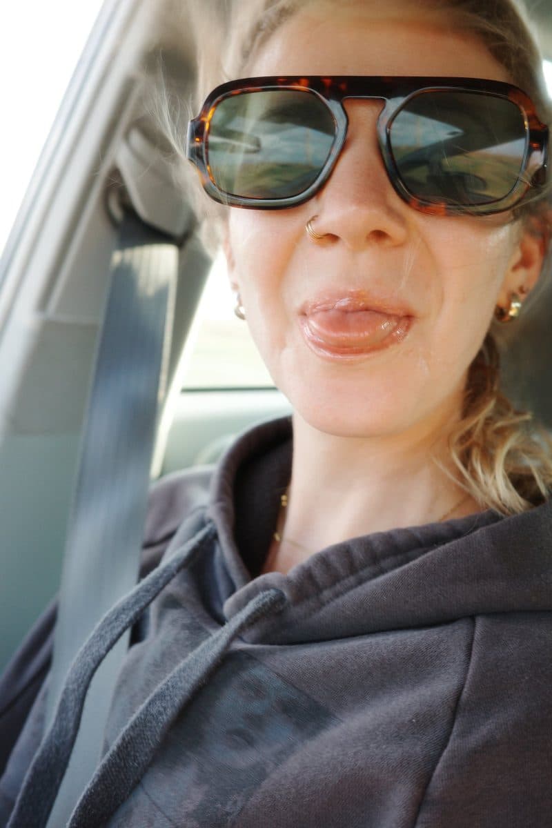 A woman in sunglasses sticks her tongue out at the camera in a car