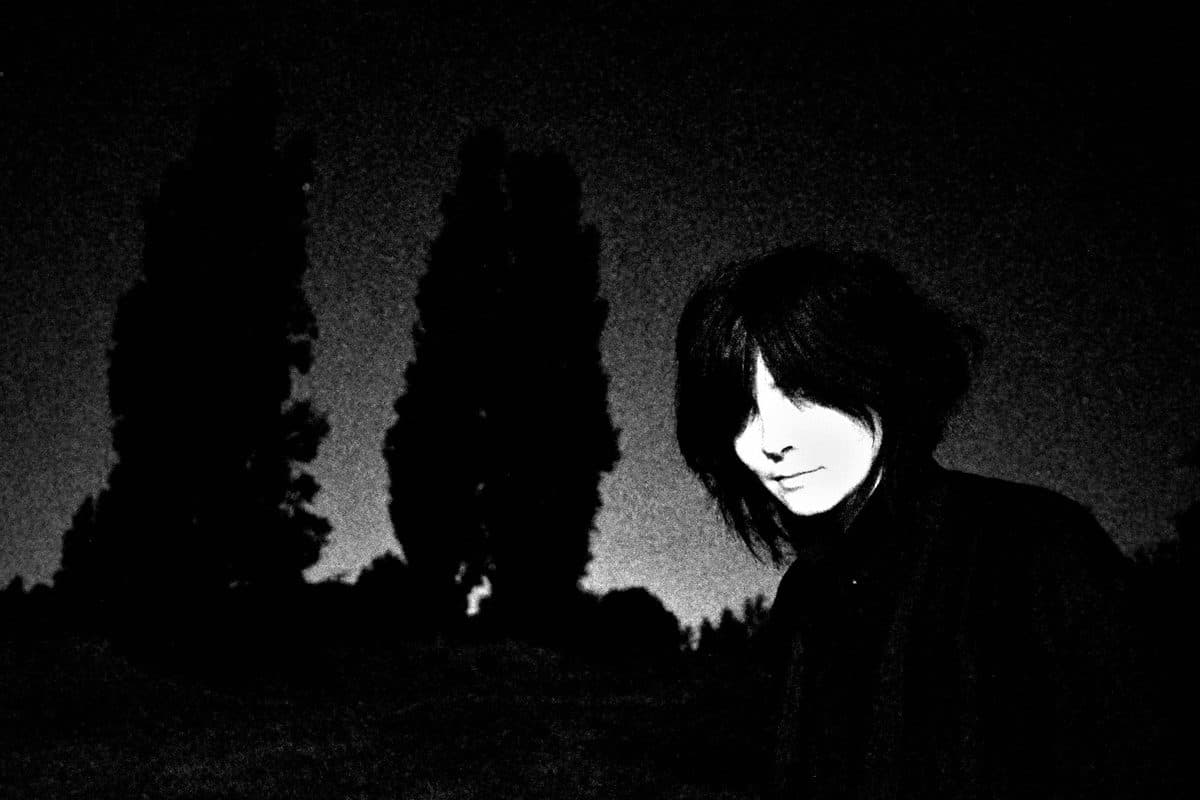 A woman at night with her hair over half her face and trees in silhouette, black and white