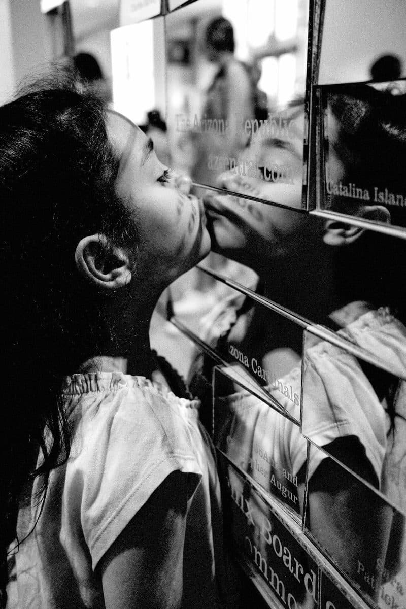 A girl kisses her reflection in a mirrored wall, black and white