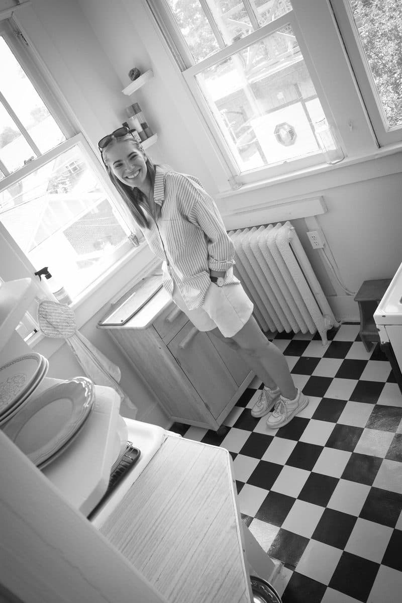 A young woman smiles in her kitchen with a checkerboard floor, black and white