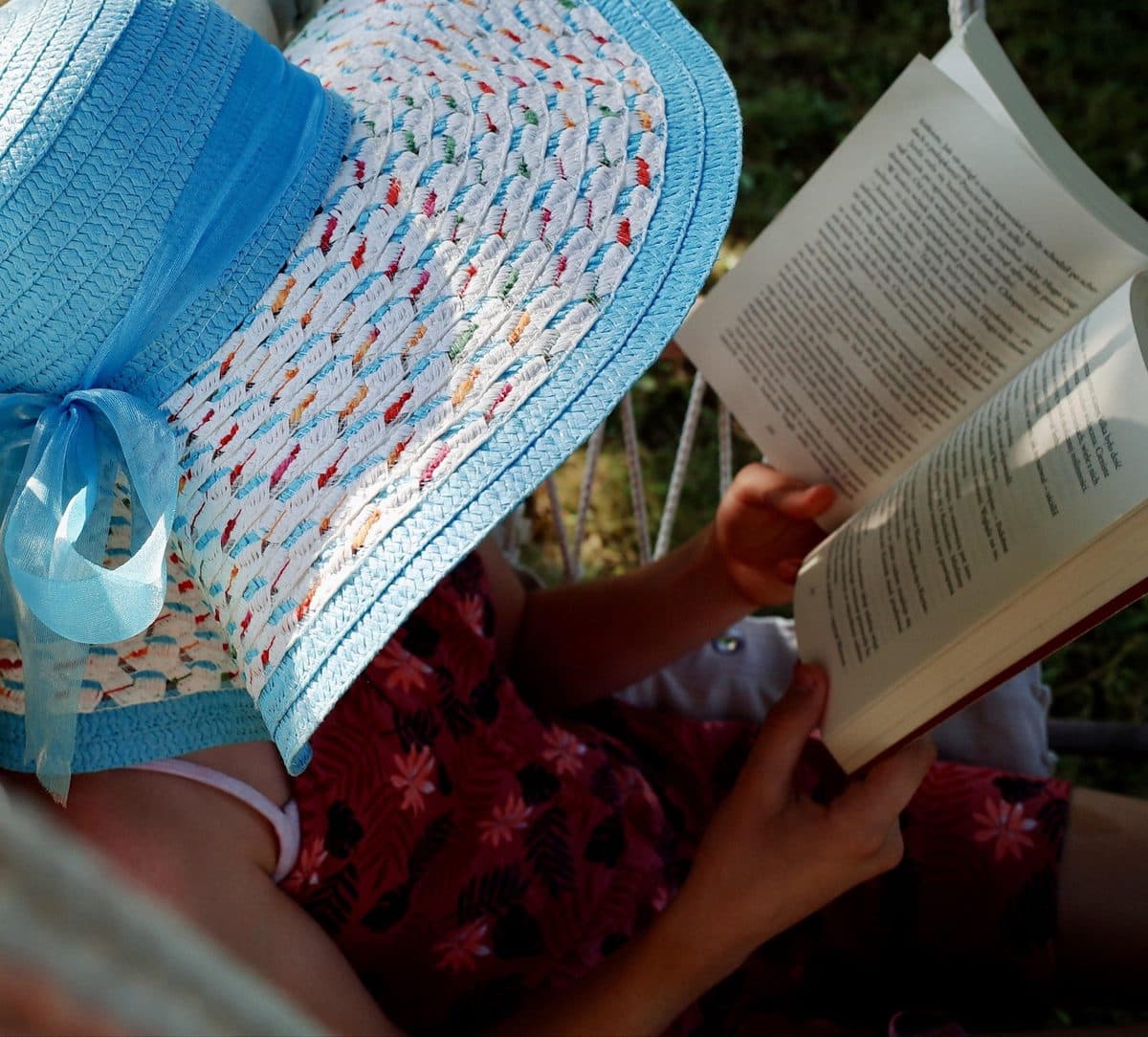 A child reads a book under a wide blue sun hat
